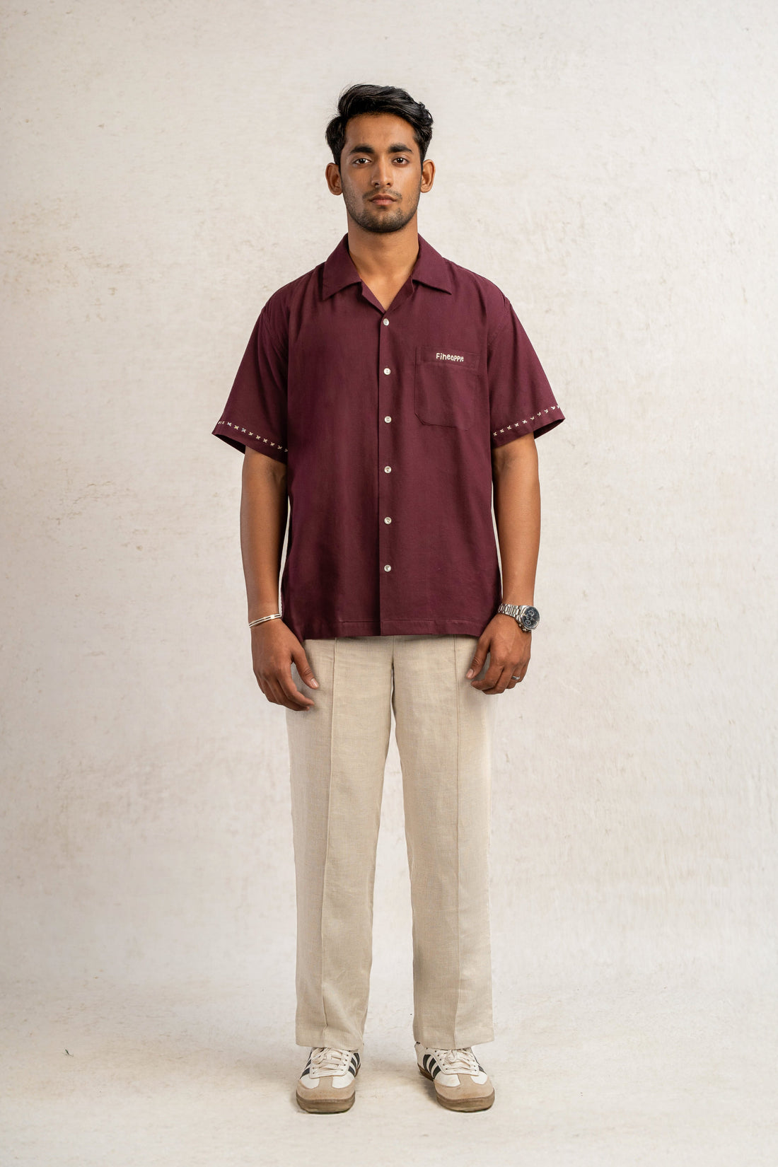 Man wearing a maroon hand embroidered shirt and beige linen pants against a plain background